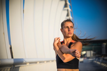 Portrait of fit and sporty young woman doing stretching in city.