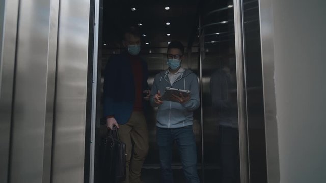 Two Men In Disposable Masks Exiting Elevator