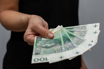 close up of one banknote with a face value of PLN 100 Polish money, zloty held  in the hands of a women on a grey background