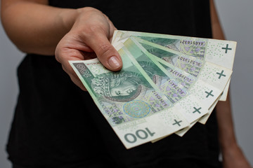 close up of one banknote with a face value of PLN 100 Polish money, zloty held  in the hands of a women on a grey background