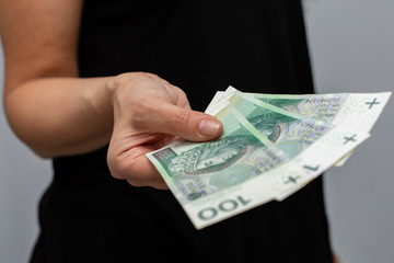close up of one banknote with a face value of PLN 100 Polish money, zloty held  in the hands of a women on a grey background