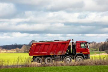 big red truck rides on a rural road on a background of green field