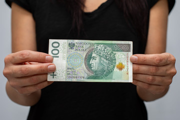 close up of one banknote with a face value of PLN 100 Polish money, zloty held  in the hands of a women on a grey background