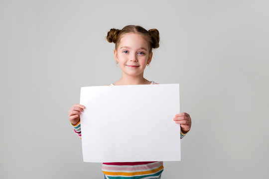 baby girl holding a white sheet.Cute little girl with a white sheet of paper.blue background.space for text.A little girl holds an empty piece of paper