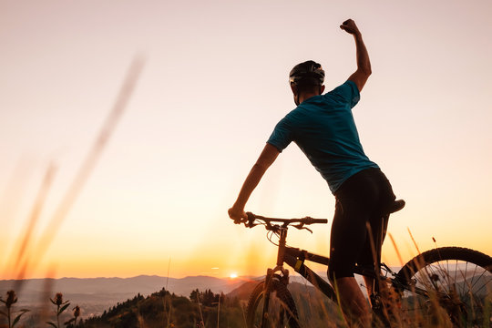 Man biker man meets a sunset in top of hill. He rising a one arm greeting on another successful day ending. Active sport people concept image