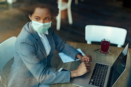 African American Businesswoman Wearing Protective Mask While Using Laptop In A Cafe.