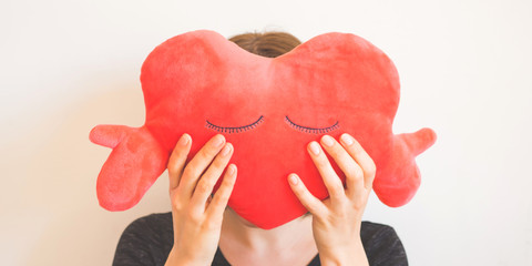 Faceless woman covering her face with red heart shaped plush toy.