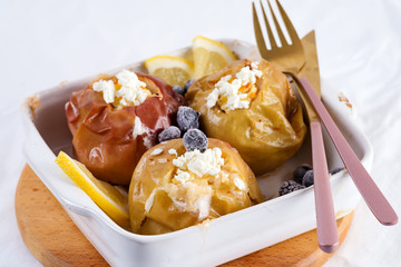 Baked apples with blueberries and cottage cheese in bowl with cutlery on white table