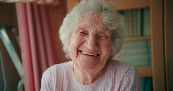 Portrait of a happy elderly woman with full white hair looking at the camera and smiling with white teeth.