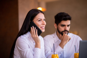 Businesswoman talking on her phone while the businessman is analyzing info on his laptop screen.