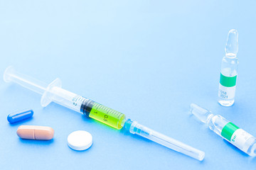 Syringe for vaccination and pills on a blue background with copyspace