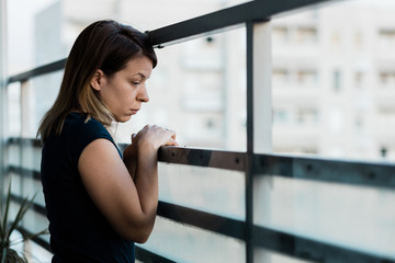 Young sad woman looking outside through balcony of an apartment building