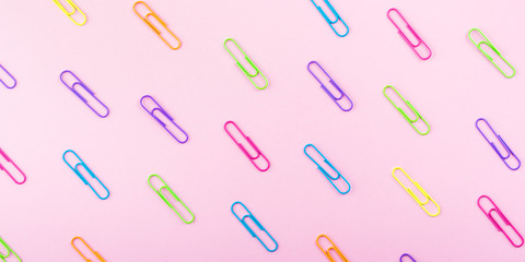Colorful clips pattern on pink paper background. Stationery flat lay web banner