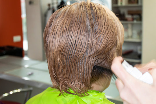 A Woman With Gray Hair Is Sitting In Front Of A Mirror In A Hairdressing Salon. The Hairdresser Does Her Hairstyle.