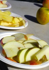 Slices of fresh apples for tasting on paper plates at an outdoor farmers market