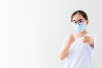Portrait Asian young woman wear a mask to protect against Coronavirus, girl raise fist and finger encourage fight contagious disease concept stop virus Covid 19 outbreak to victor on white background