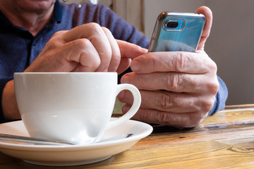 Men's hands hold a smartphone. Reads the news, dials a message at a table in the cafe with a cup of...