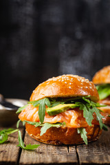 Burger sandwich with salmon, cream cheese, avocado and arugula on a light background, concept diet food, sandwich take away, healthy fast food