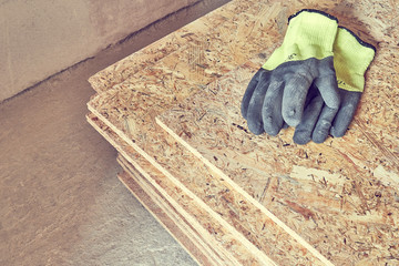 OSB slab building material made from reborn sawdust. They lie in a pile, yellow protective gloves lie on it. Close-up