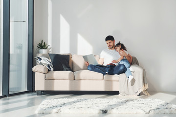 Happy father with his daughter spending free time with laptop at home together