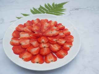 Red strawberry ripe piece slice of shape heart in a white dish (plate) with green leaves on the...