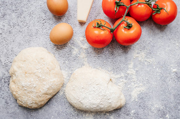 wholemeal dough ball for homemade pizza made on an abstract stone background with ingredients around, tomato, flour, cheese and egg