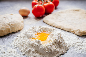 wholemeal dough ball for homemade pizza made on an abstract stone background with ingredients around, tomato, flour, cheese and egg