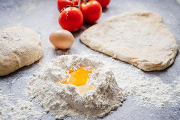 wholemeal dough ball for homemade pizza made on an abstract stone background with ingredients around, tomato, flour, cheese and egg
