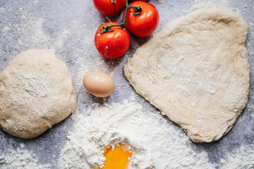 wholemeal dough ball for homemade pizza made on an abstract stone background with ingredients around, tomato, flour, cheese and egg