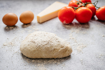 wholemeal dough ball for homemade pizza made on an abstract stone background with ingredients around, tomato, flour, cheese and egg