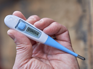 Male hand holds clinical thermometer with corona text on the screen during global covid-19 or corona pandemic