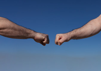 Two male hands on a blue background almost fist bumping, keeping a safe distance