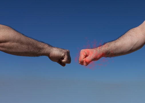 Two male hands on a blue background almost fist bumping, keeping a safe distance, one covered with virus, concept