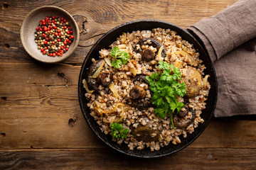 Buckwheat porridge with mushrooms in the frying pan on wooden table, top view