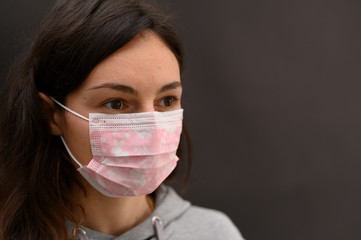 Cute young brunette girl in a disposable medical mask on a dark background. A look to the side. Horizontal view.