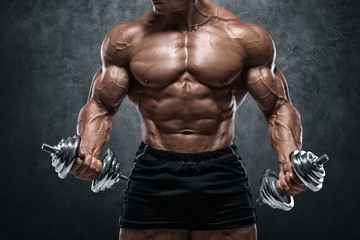 Muscular man working out with dumbbells, isolated on wall background. Strong male naked torso abs