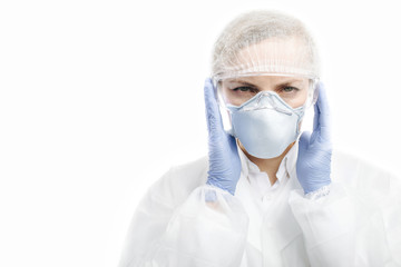 Portrait of mature woman in protective glasses, mask, medical hat and blue rubber gloves looking at camera with serious facial expression. Isolated over white studio background.