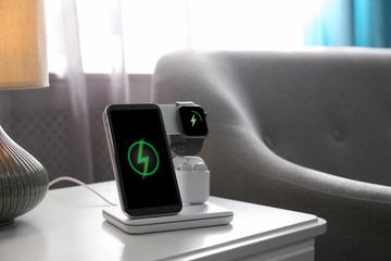 Smartphone, watch and earphones charging on wireless pad in room. Space for text - obrazy, fototapety, plakaty