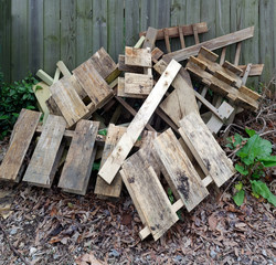 Jumbled heap of junk wooden palettes in neighborhood alley against fence.