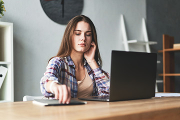 Pretty woman working with laptop, making notes and thinking