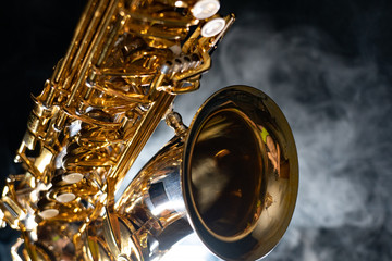 Golden shiny alto saxophone on black background with smoke. copy space