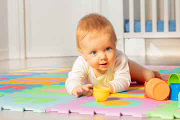 Beautiful baby toddler boy, lay and crawl in front of crib play reaching toys on the carpet