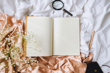 Spring composition, white gypsophila flowers with notebook and magnifying glass on the gold satin...