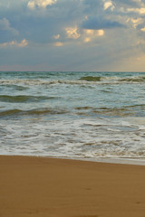 Sandy beach with waves and foam as a natural background with reflection of sunlight on water. Summer holiday concept.