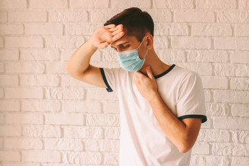 Portrait of young sick man in medical protective mask suffering from high body temperature. Man ill...