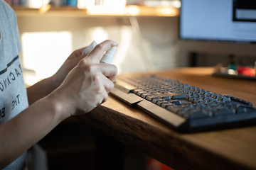 Women hands using alcohol spray and wiping down surfaces on a computer keyboard for cleaning and protect COVID-19