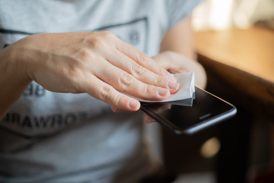 Woman Cleaning Her Smart Phone By Spray And Wiping Down Surfaces.