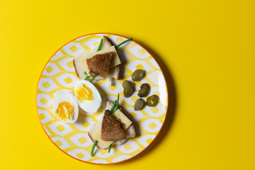 Plate with open sandwiches with cheese and meat, boiled egg, green onion, marinated pepper on yellow background