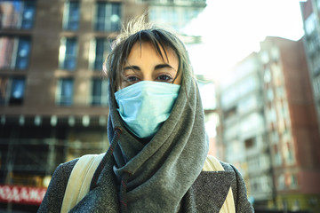 Close-up portrait woman in hood with face maskstanding in front of buildings on street with...
