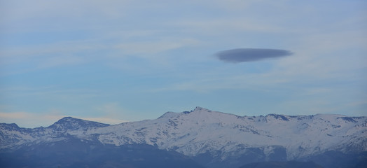 Fototapeta na wymiar Lonely black cloud over Sierra Nevada with snow at sunset